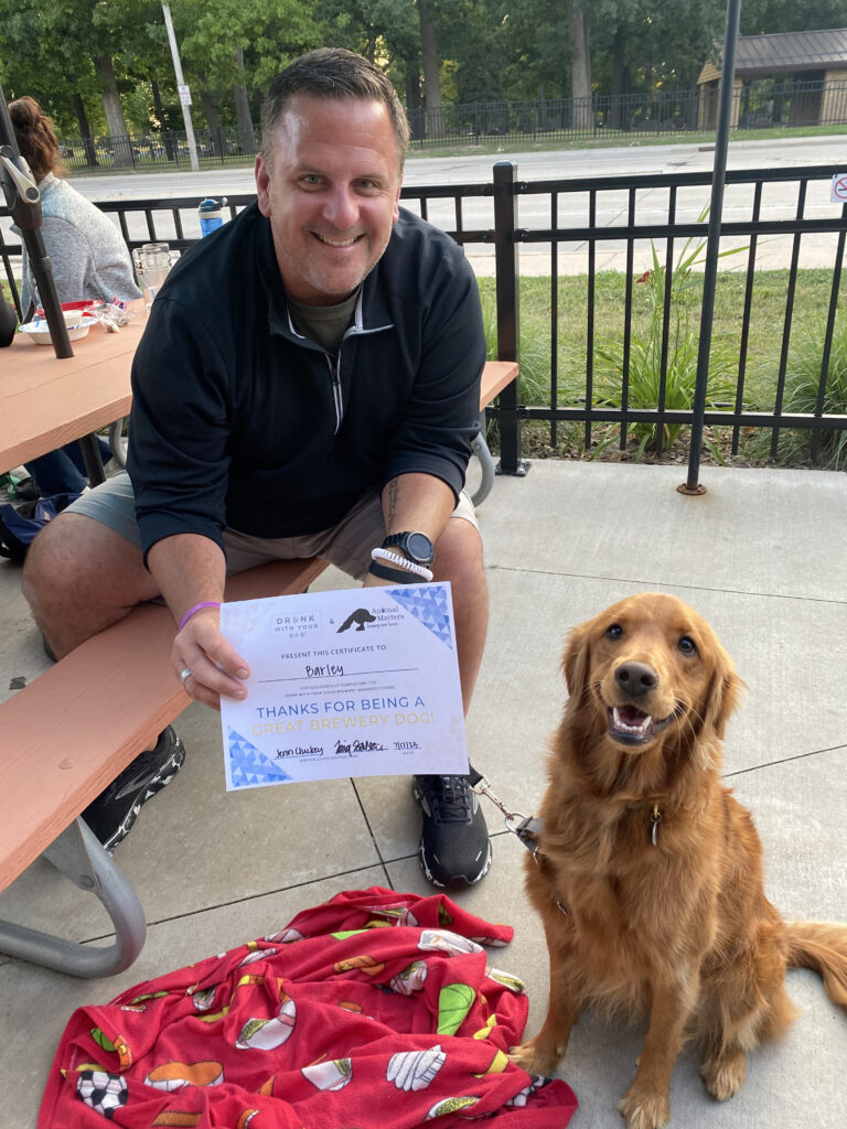 Golden Retriever and owner smile at the camera with a brewery manners group class graduation certificate